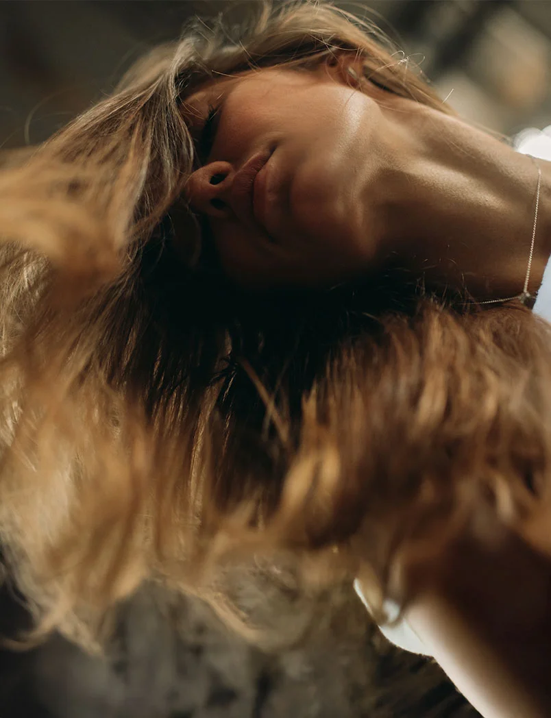 A beautiful woman with her head tilted back and her eyes closed, looking serene and relaxed. Her blonde hair is cascading around her head, creating a soft, blurry foreground. The image is focused on her peaceful expression, suggesting a state of rest, beauty, and tranquility. - Kybella in Greenwood Village, CO